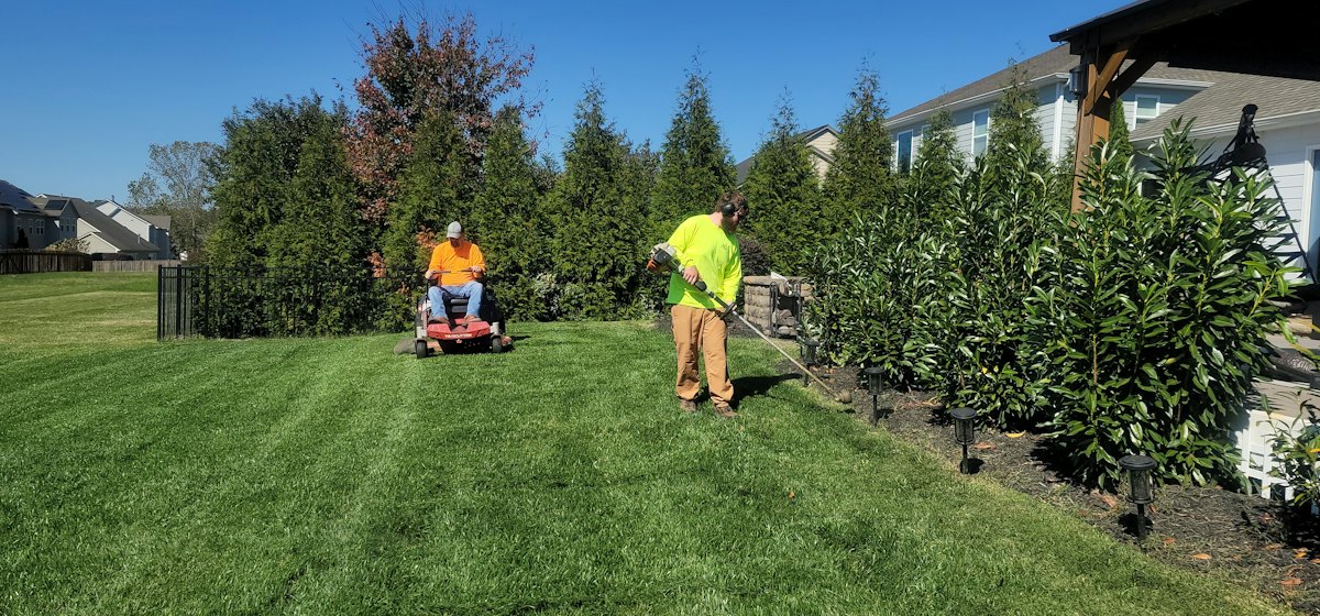 Two gardeners mowing and trimming a large lawn