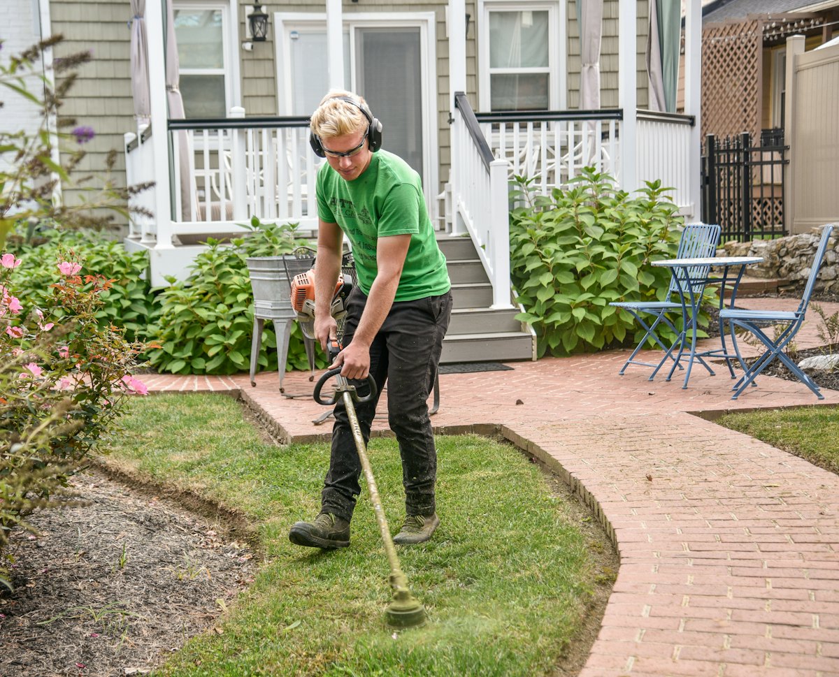 A gardener trimming the lawn edge beside a brick path
